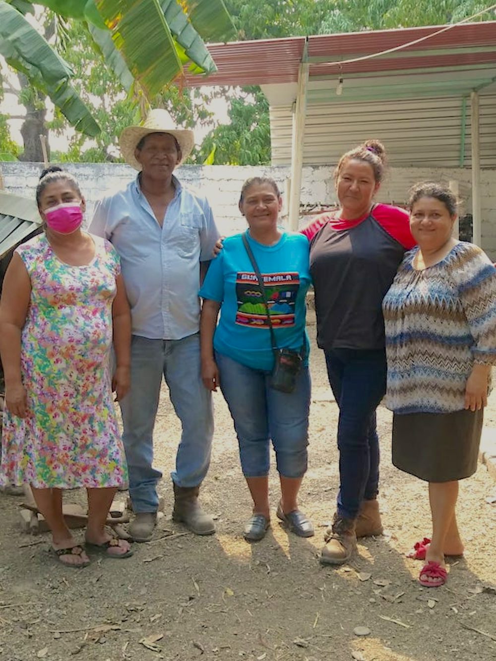 Four members of the cooperative, three women and one man, stand side by side in a chicken coop.