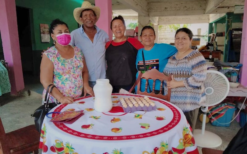 Five members of a chicken cooperative stand around a table, all smiling at the camera.