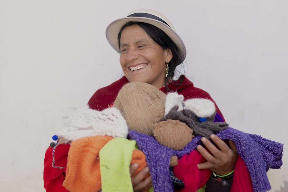 An Ecuadorian woman holding an armful of knitted goods and laughing.