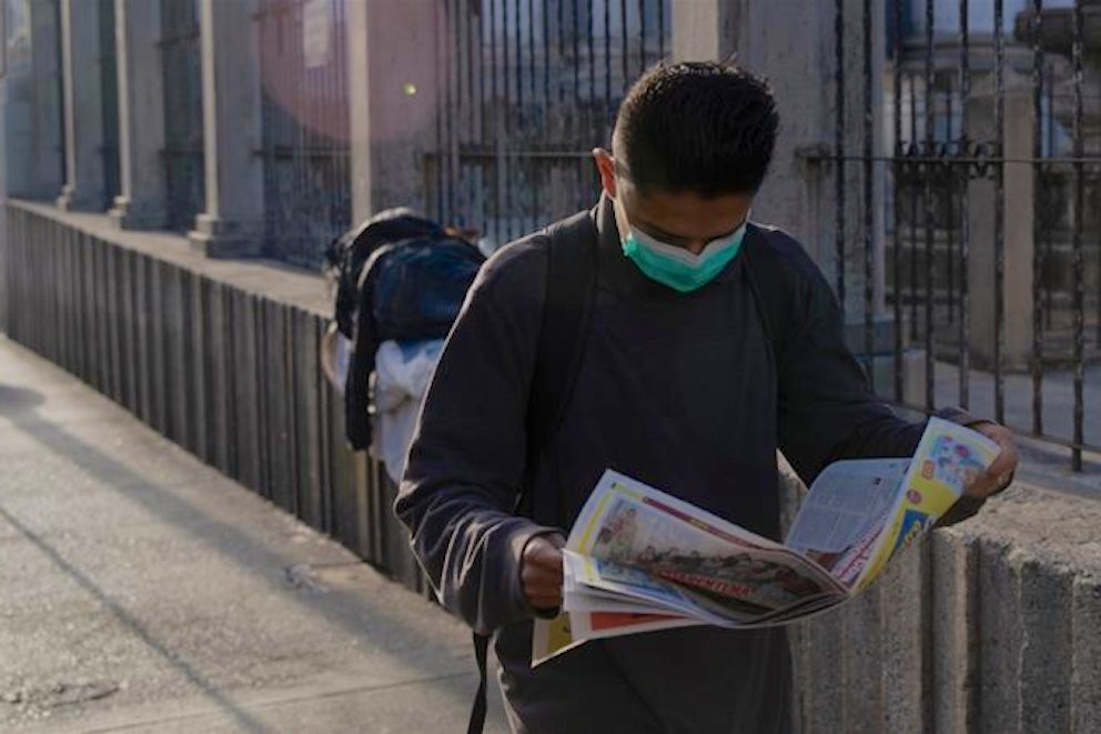 A Guatemalan man wearing a face mask looks down at the newspaper he is reading