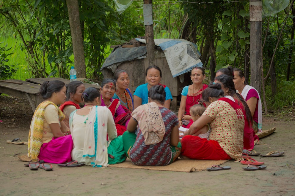 A group of women in Nepal sit in a circle on a mat, discussing their farms.