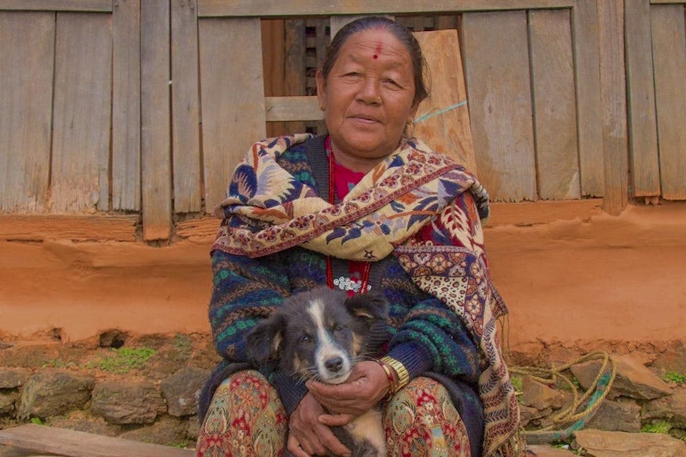 A middle-aged woman, Til Kumari Gurung, sits and looks at the camera, holding a black and white puppy.