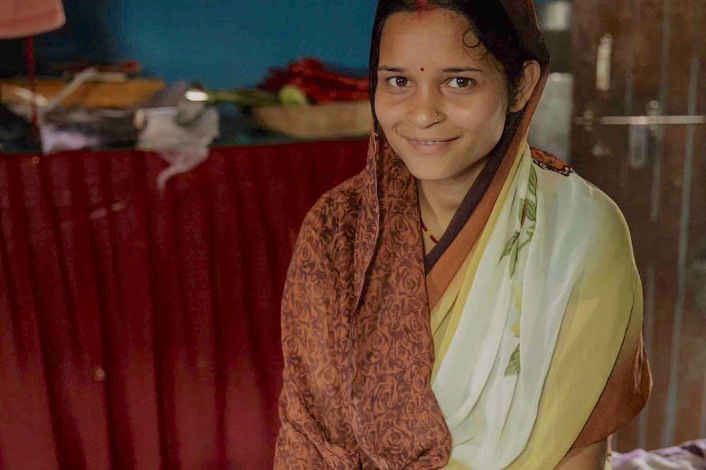 Puja Devi sits on her bed with a textbook open in front of her.
