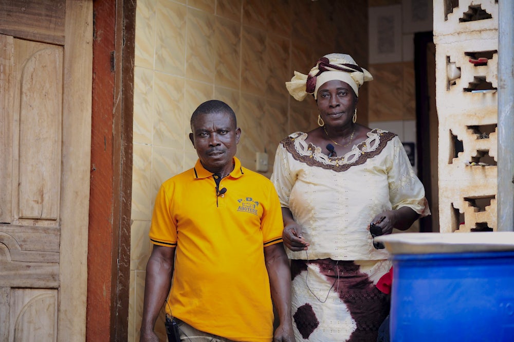 Rose stands beside her husband in the entryway of their home in Ghana