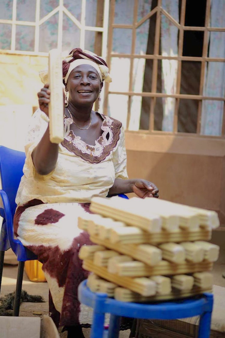 A sitting Ghanese woman proudly holds up a bar of soap she made for her growing business.