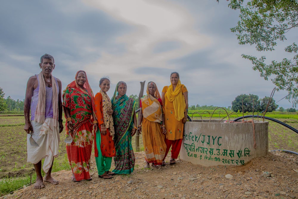 A group of six Nepali farmers stand beside a well near a vegetable field.