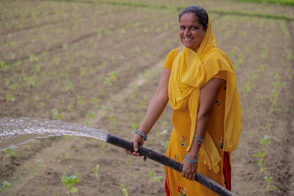 A Nepali woman wearing bright yellow garbs waters her vegetables with a hose.