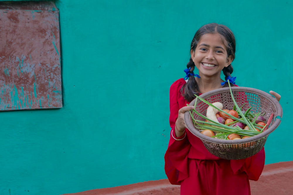 A girl holds a bowl of fresh produce.