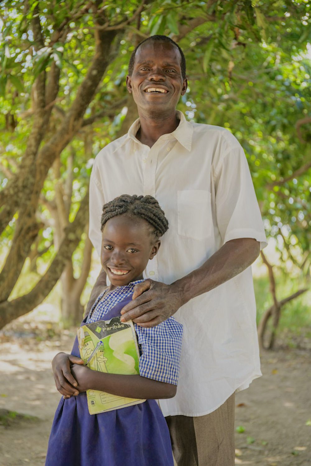 A father stands with his young daughter on her way to school.