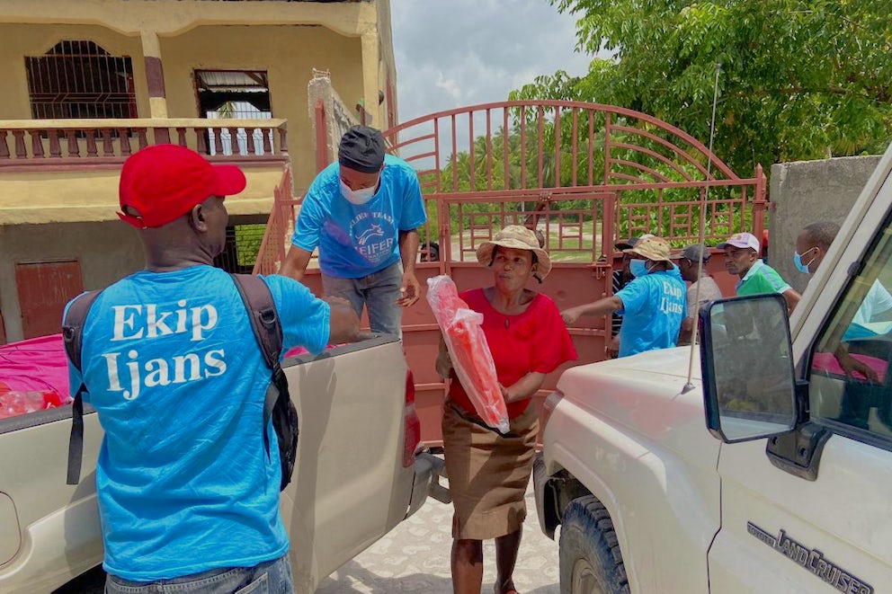 Two Heifer employees distribute orange tarps to Haitian residents from the back of a truck.