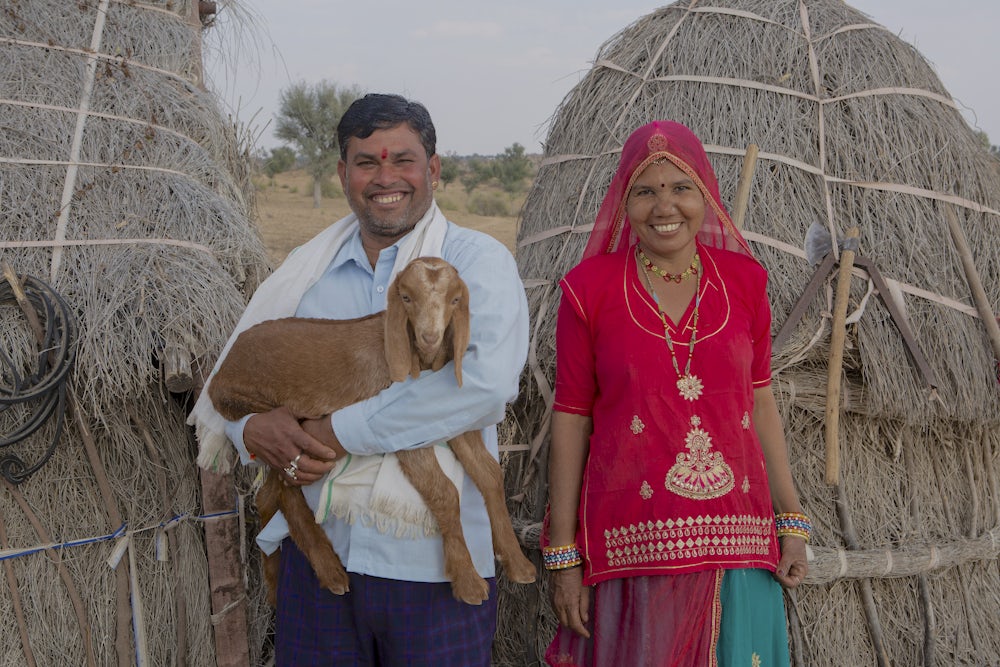 An Indian couple stand together holding one of their goats.