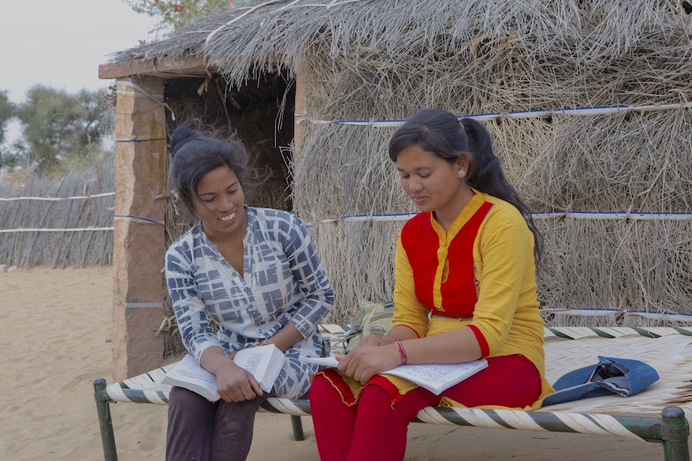 Two Indian teenage girls sit together and read books in the state of Rajasthan.