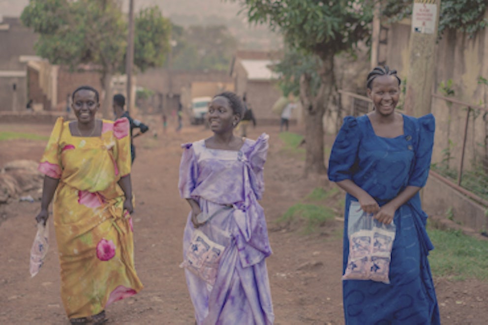 Three smiling women walking in a dirt street