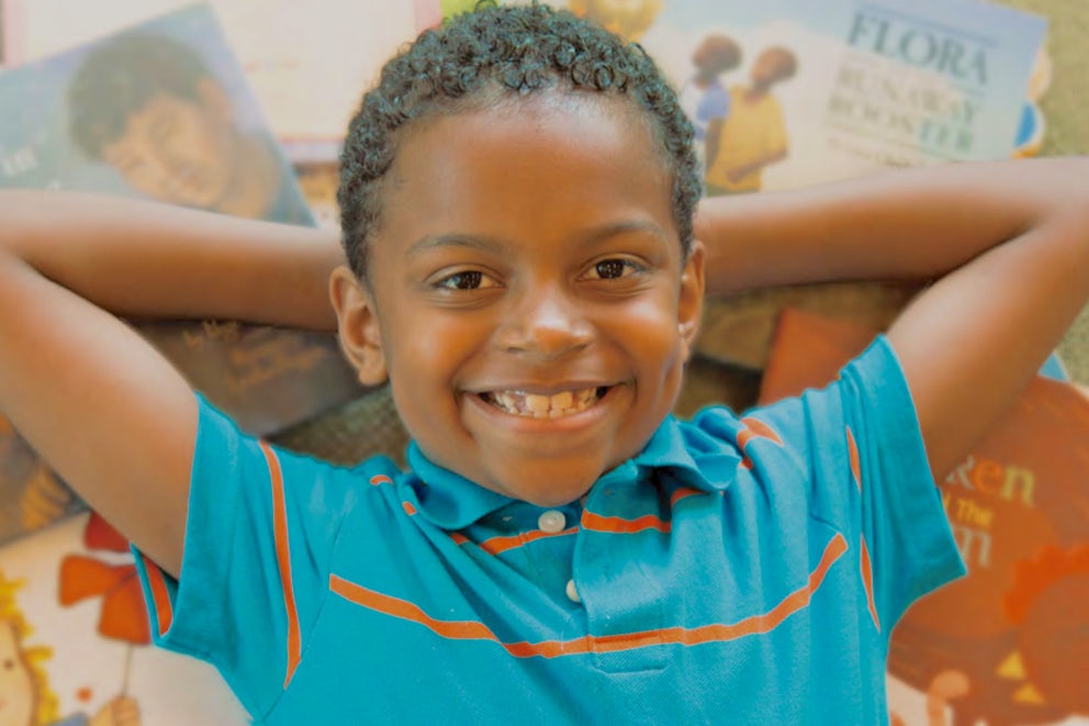 Child laying on books smiling.