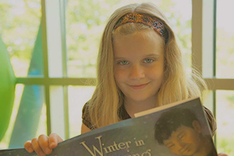 Child reading book, Winter in Songming, smiling at camera.