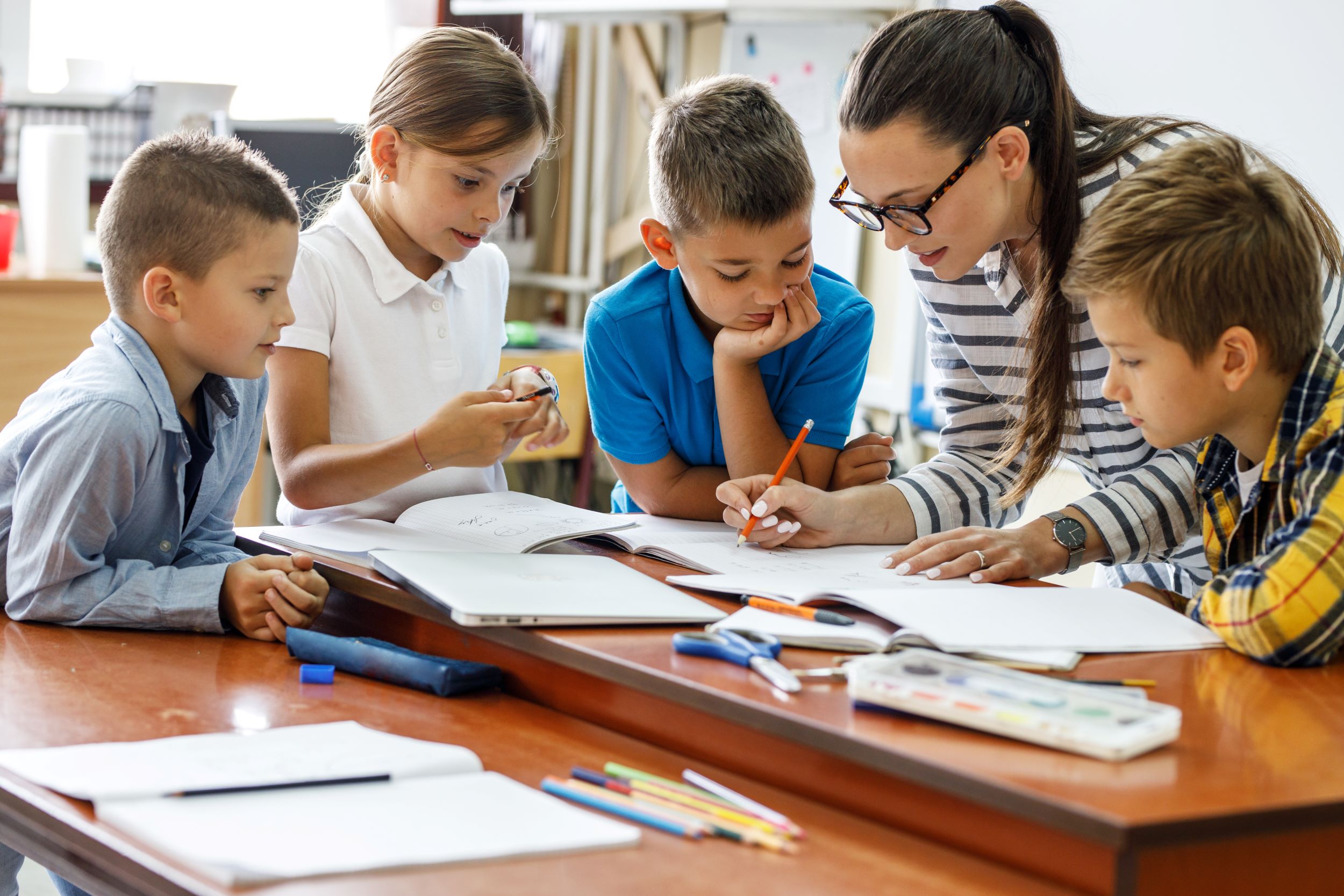 Teacher surrounded by students while writing in notebook
